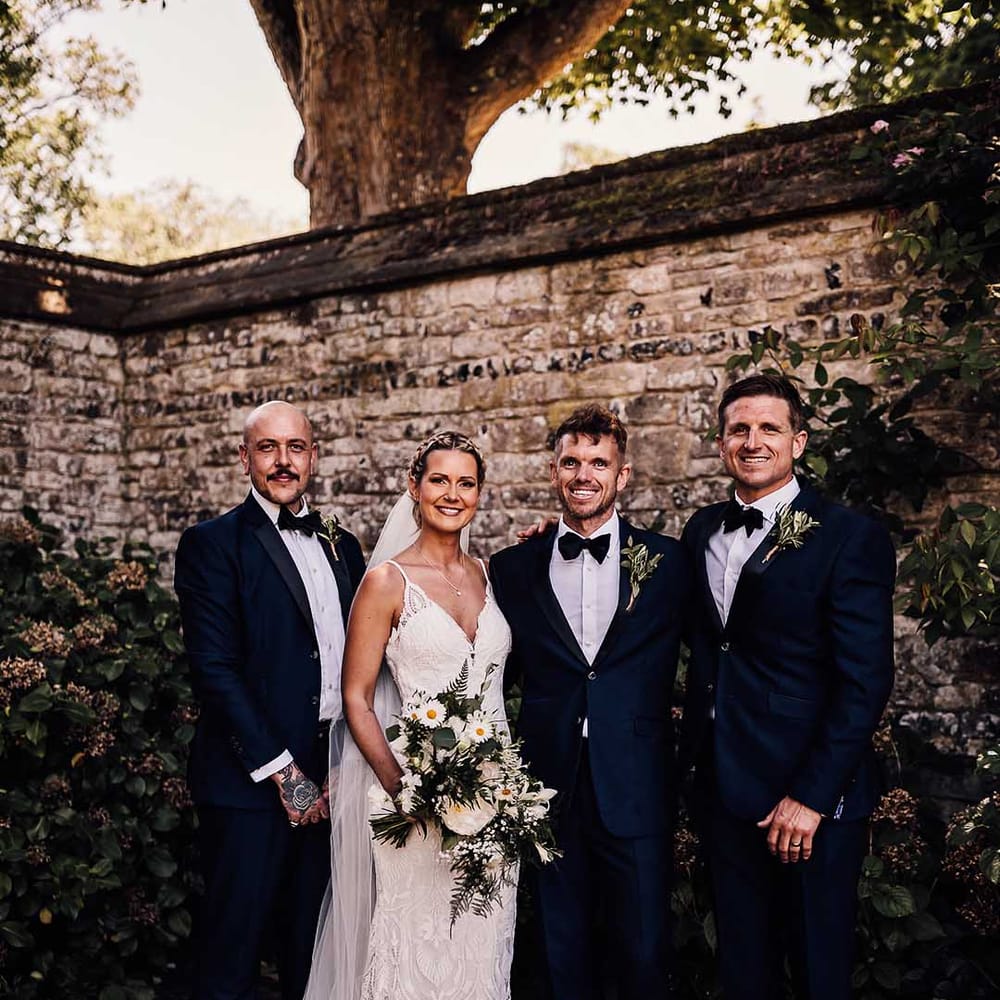 Bride in white lace wedding dress with white flower bouquet and groomsmen in matching blue tuxedo 