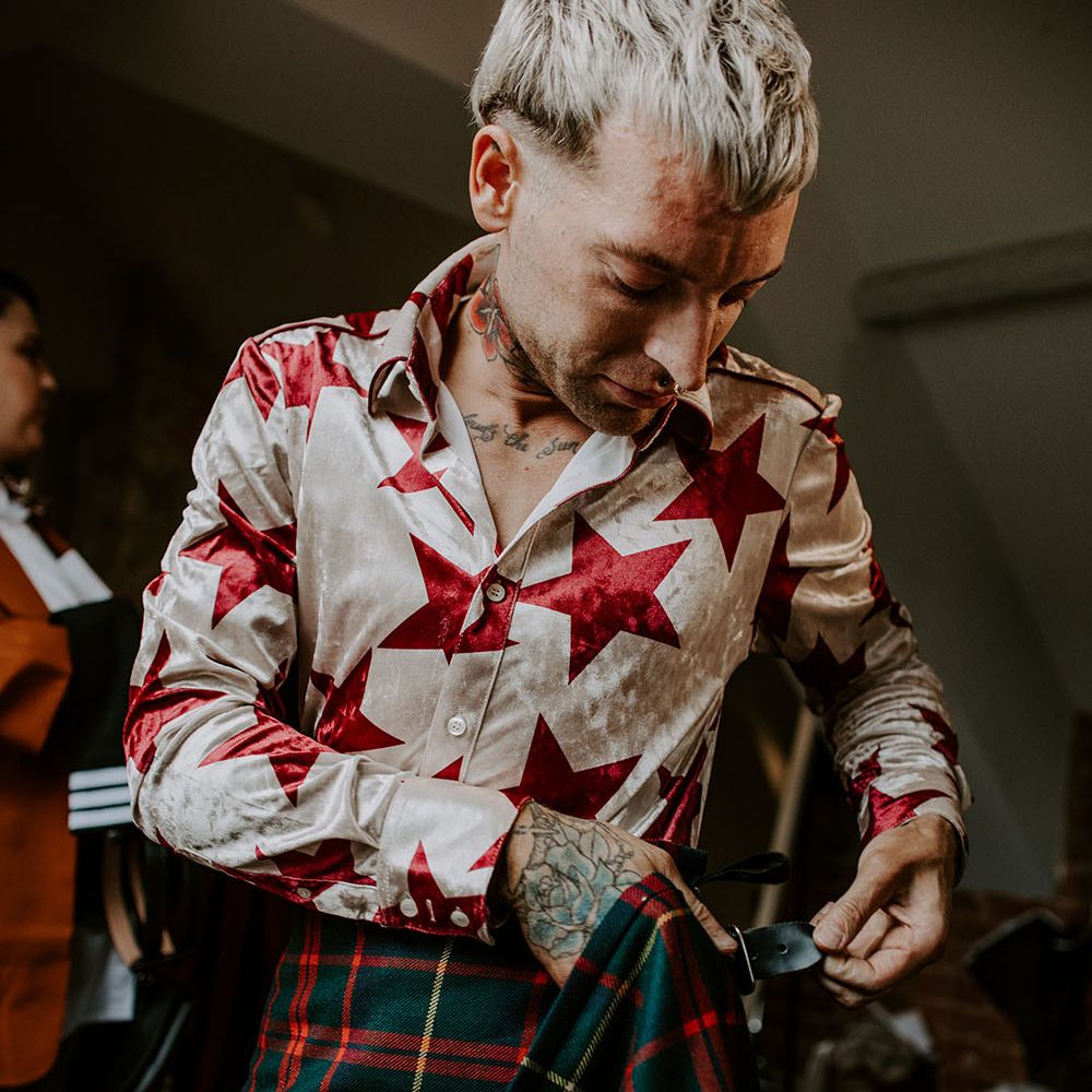 Groom wears white and red star shirt tucked into Tartan kilt on the day of his wedding 