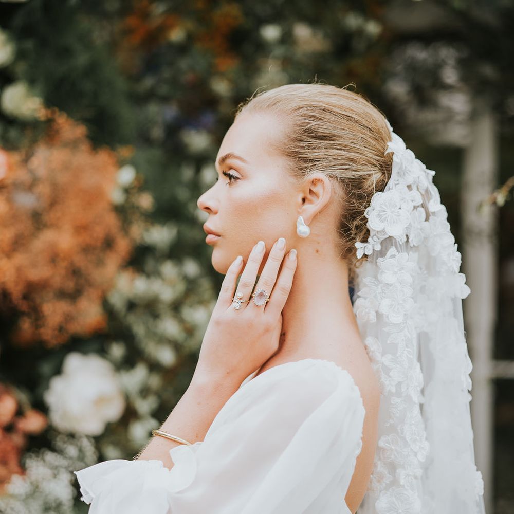 Bride with a flower wedding veil, pearl earrings, and pale pink rings 