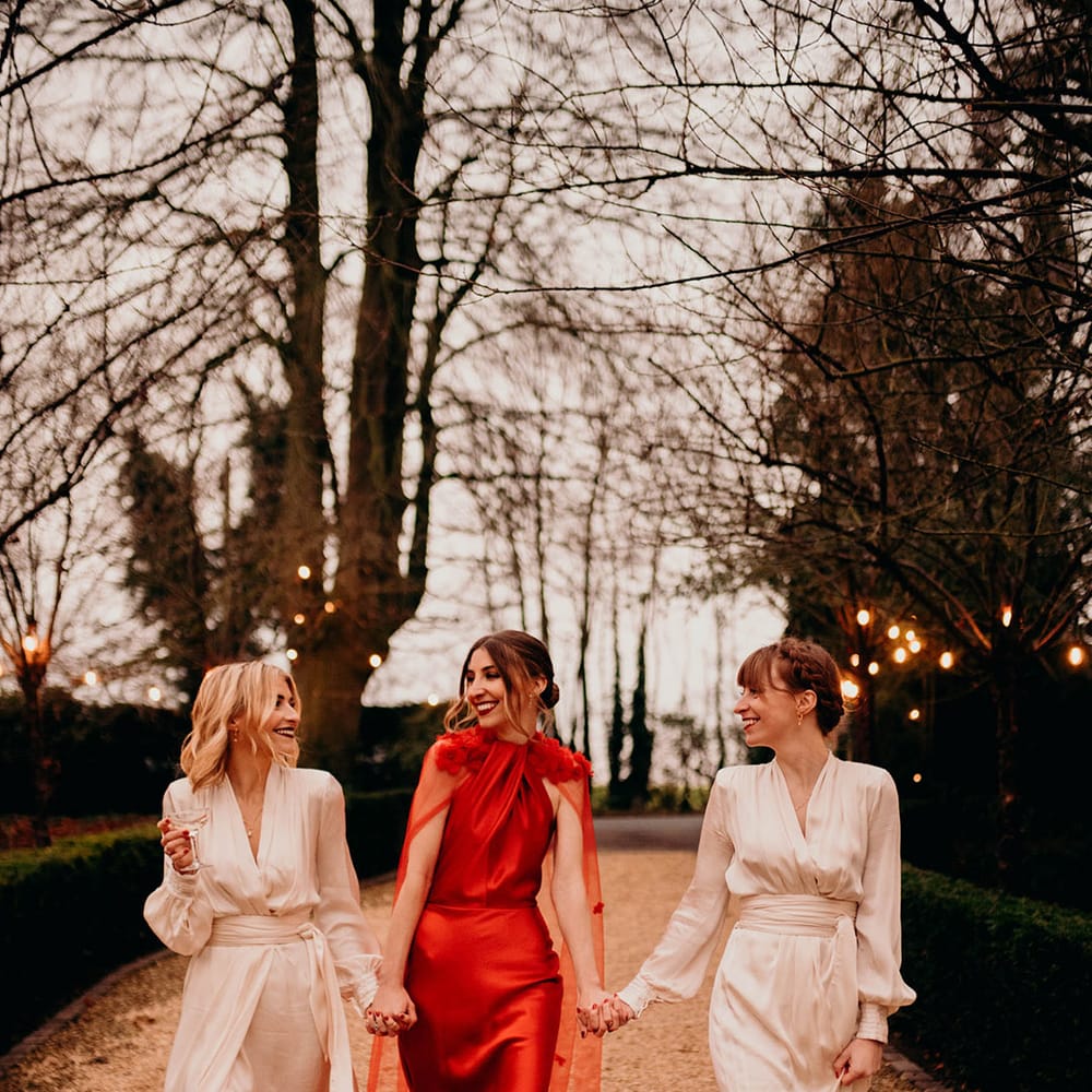 Bride in red satin wedding dress with cape and bridesmaids in ivory long sleeve wrap bridesmaid dresses