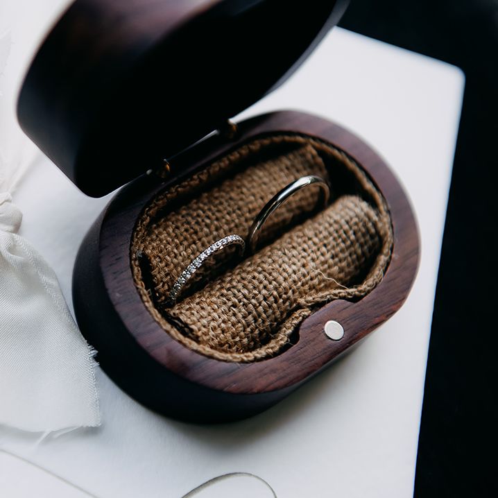 Mahogany wedding ring holder with brown garter stitching and two rings, one silver, the other silver with diamonds