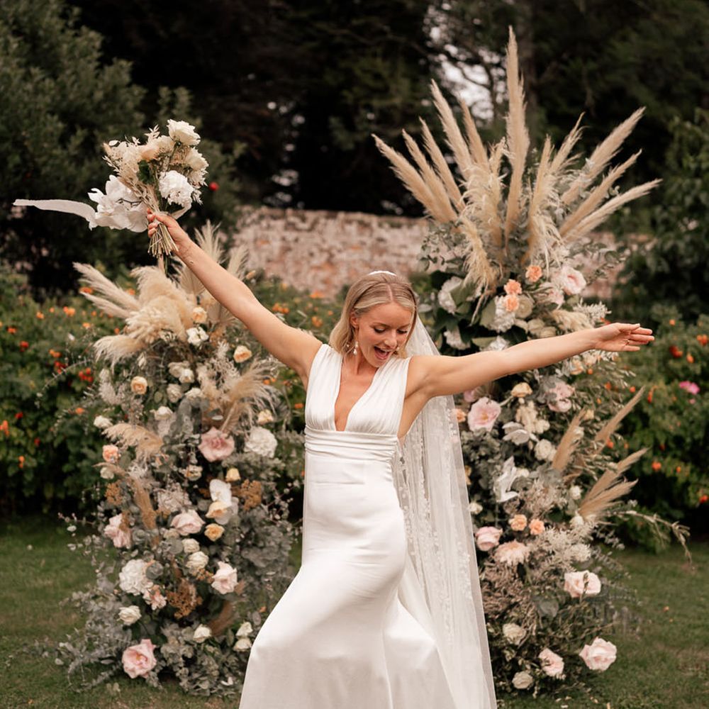 The bride poses in front of two tall flower columns with pampas grass 