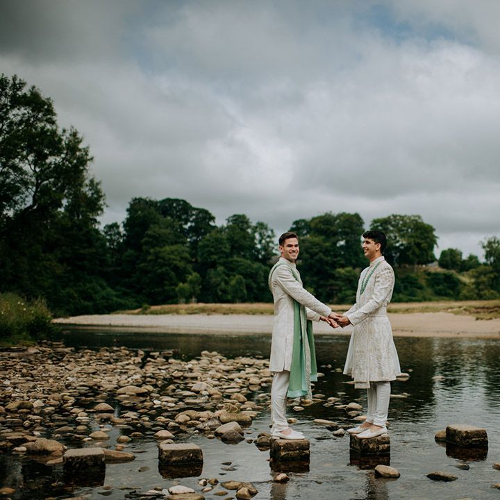 Grooms stand beside lake on their wedding day for couples portraits outdoors 