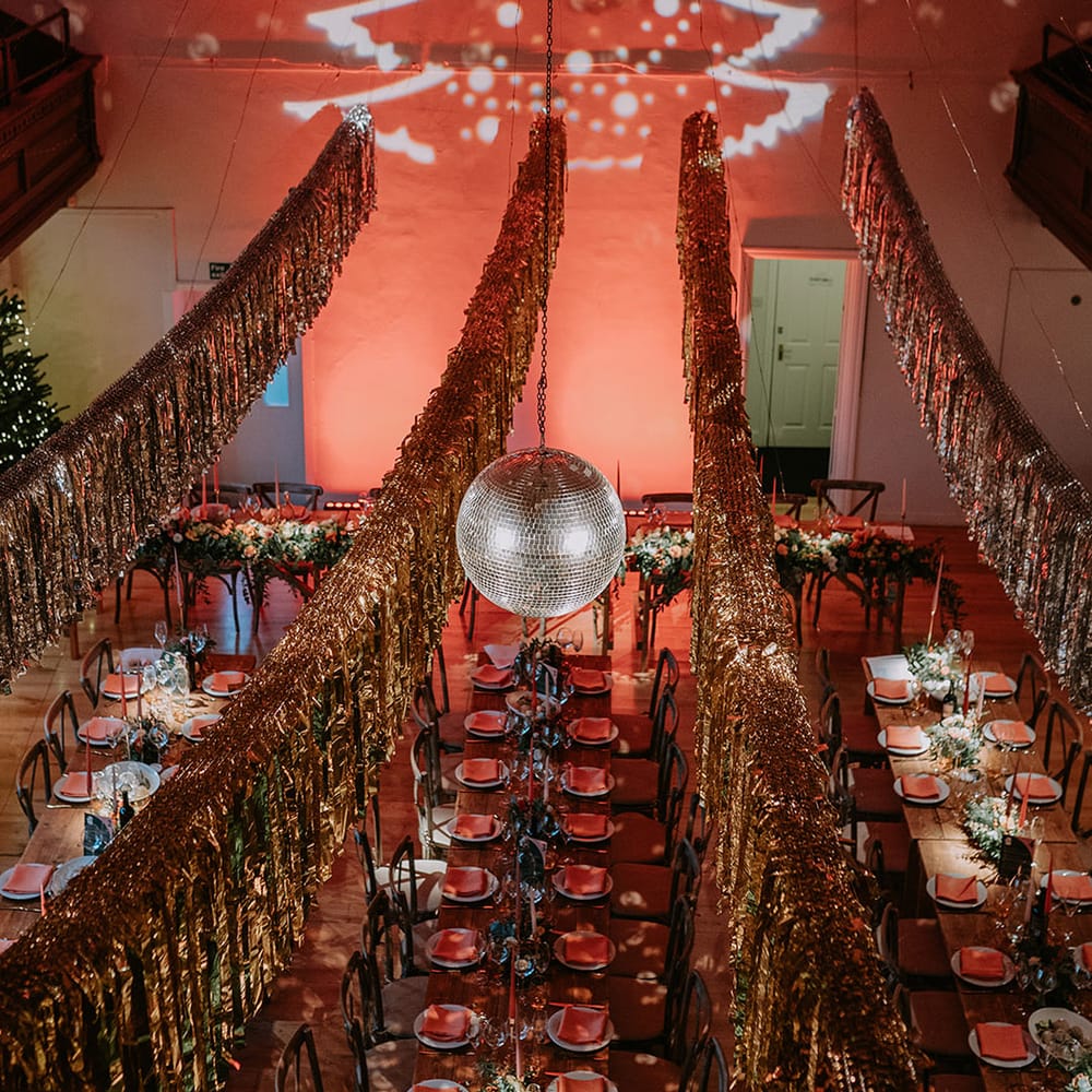Gold wedding streamers, Christmas tree projection, large hanging disco ball and Christmas themed wedding tablescapes in reception room of London wedding venue 