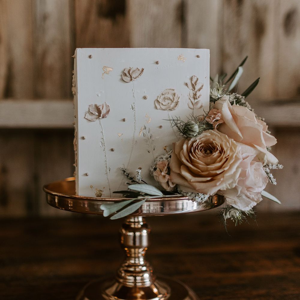 Close up of the square wedding cake with pink iced flowers on and real roses on gold cake stand 