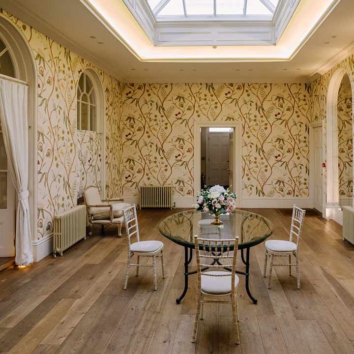 One of the rooms in Braxted Park wedding venue with light yellow floral wallpaper and luxe cream and gold furniture 