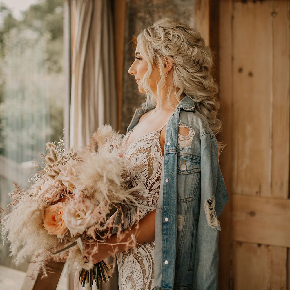 Bride with intricate braided wedding hair in lace wedding dress and light blue bridal denim jacket 