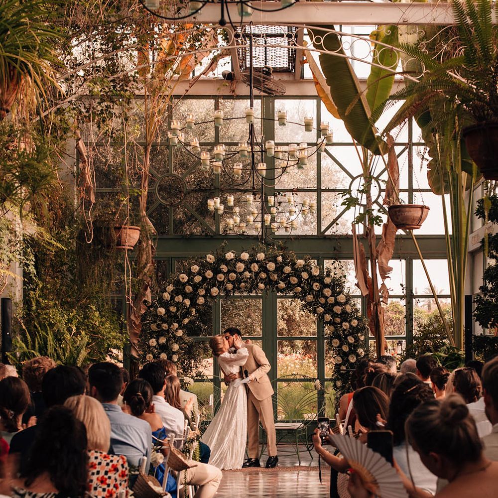 Bride and groom share romantic first kiss as a married couple in front of the white rose floral arch altar decor 