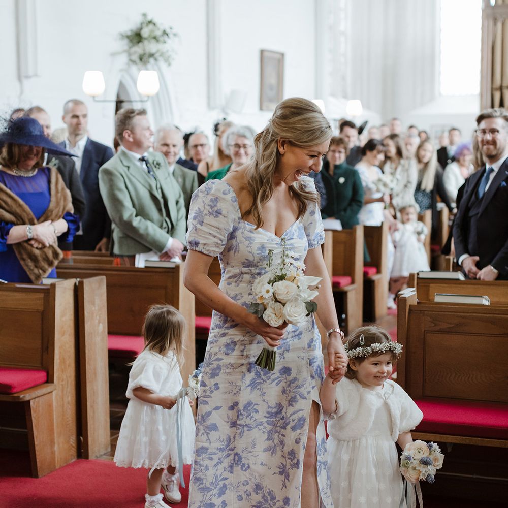 Flower girls in white dresses walk down the aisle with bridesmaids at church wedding 