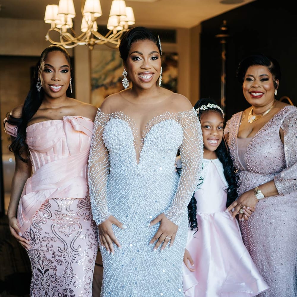 Bride in illusion v neck sheer off shoulder long sleeve pearl embellished wedding gown standing with bridesmaids in mismatched pastel bridesmaid dresses and flower girl in baby pink flower girl dressand white cardigan 