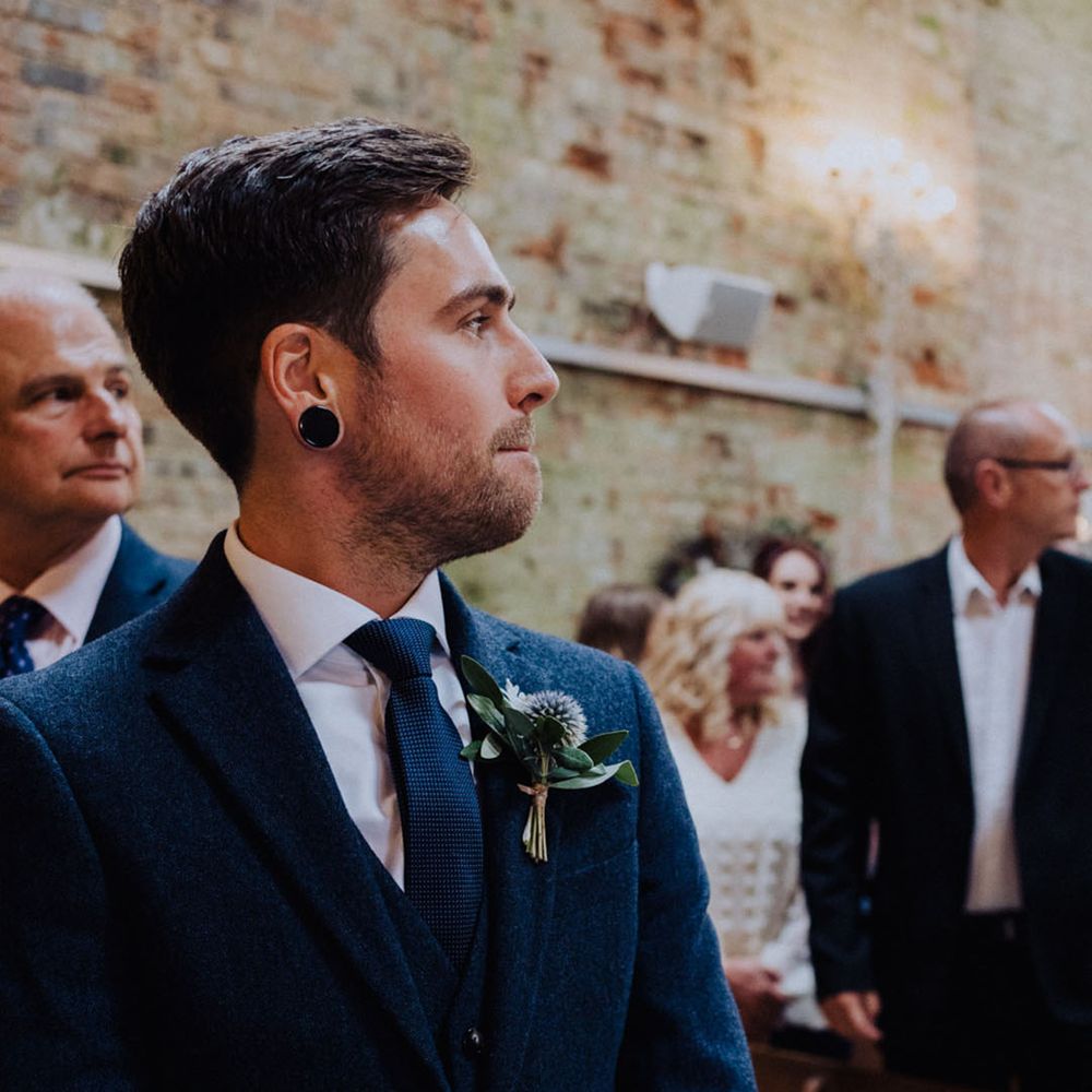 Groom in dark blue wedding suit and matching tie with thistle buttonhole 