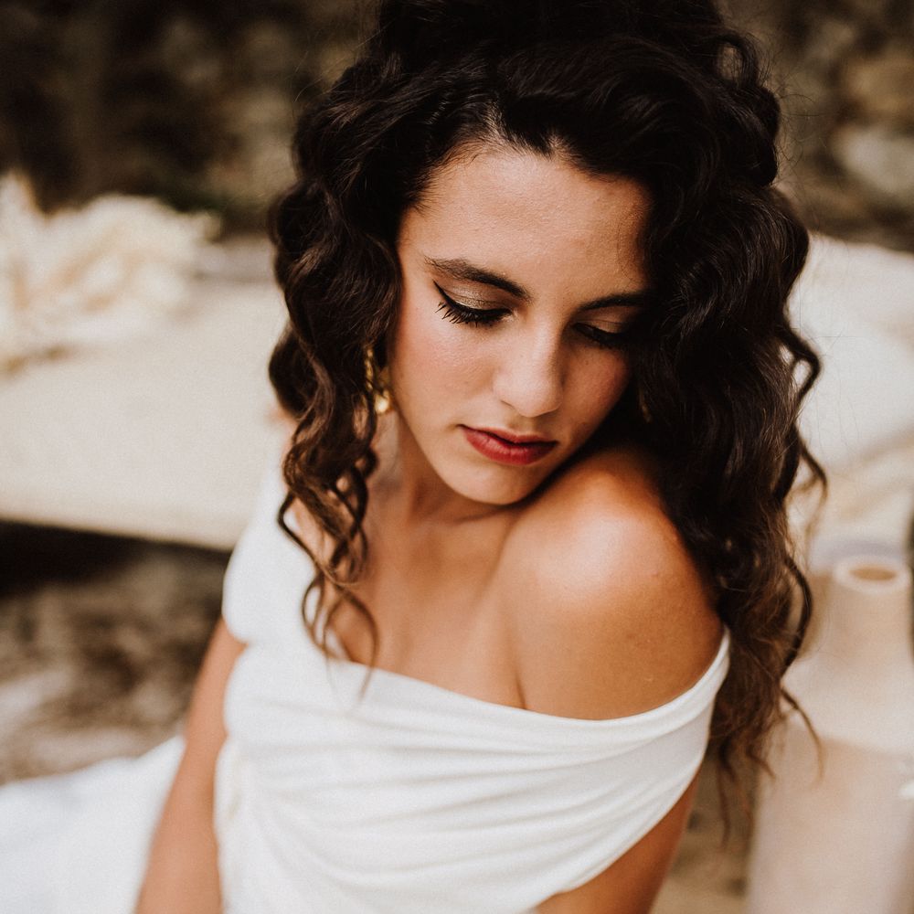 Boho bride wearing white off the shoulder gown with dark crimped hairstyle