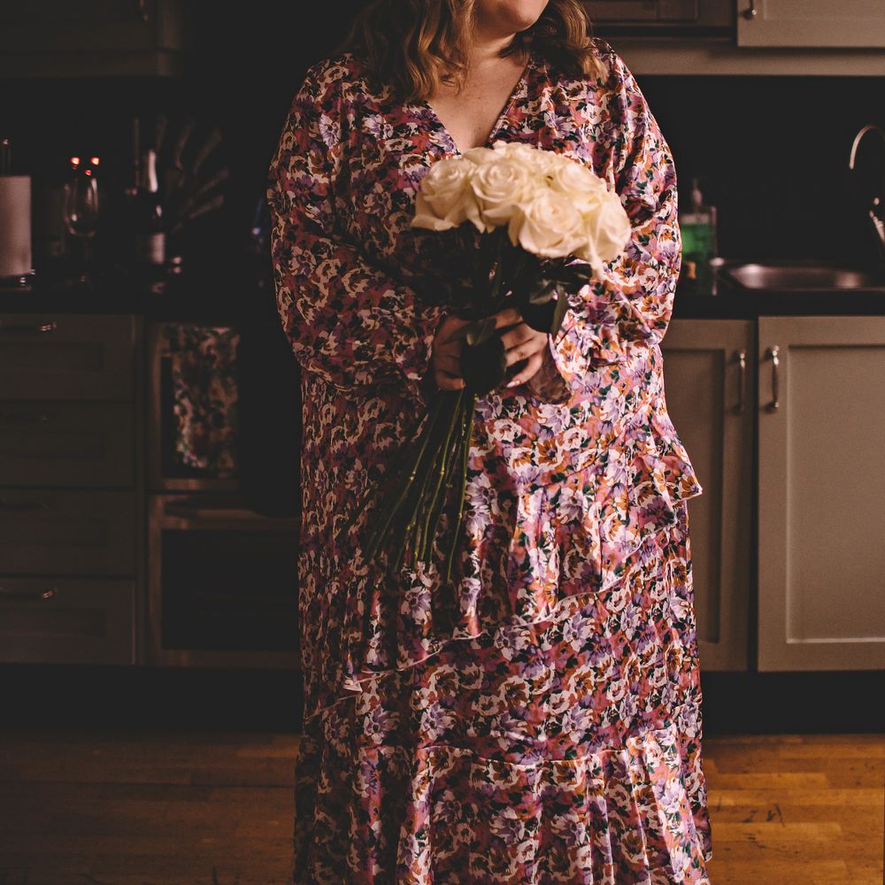 Bride holds long stemmed white rose bouquet whilst she wears floral ASOS wedding gown
