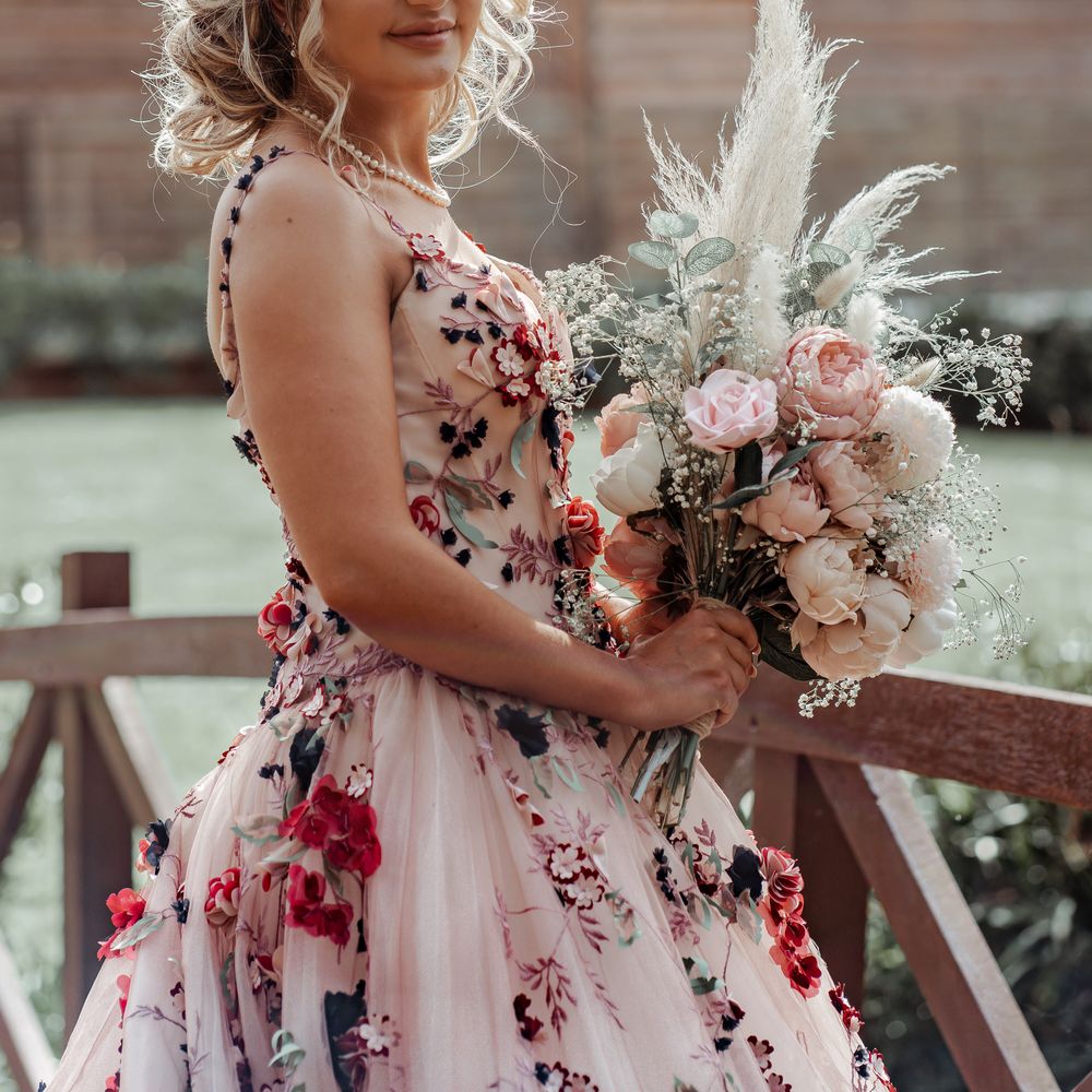 Bride wears floral appliqué wedding gown with blush pink colouring and carries floral bouquet