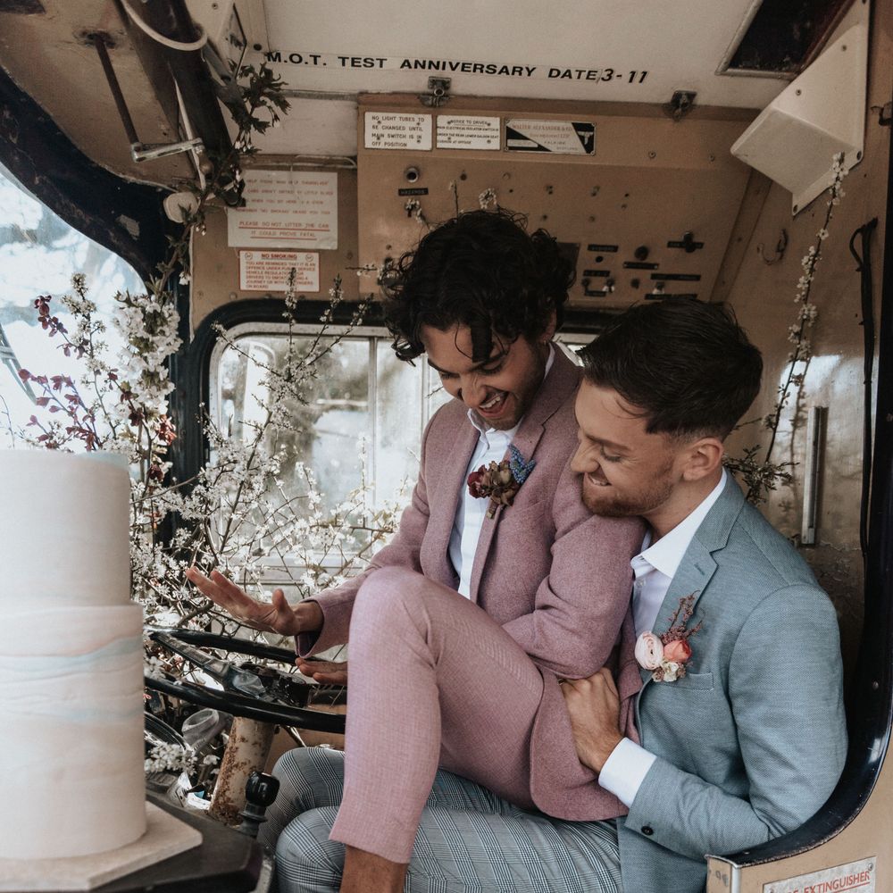 Grooms sit with one another at rustic venue on their wedding day