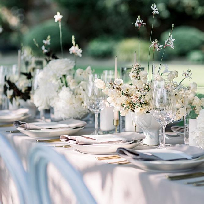 Elegant outdoor tablescape with white tableware, and flower centrepieces 