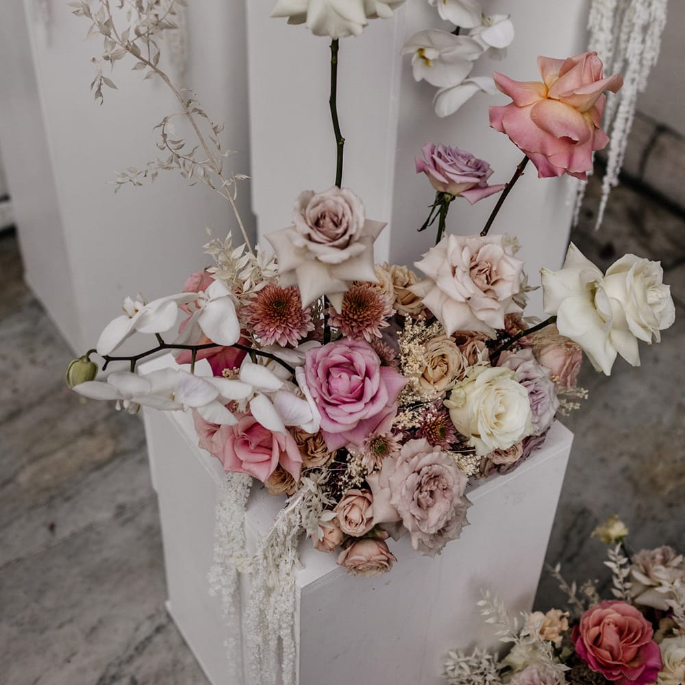 blush pink and white rose and orchid floral arrangement resting on a white plinth 