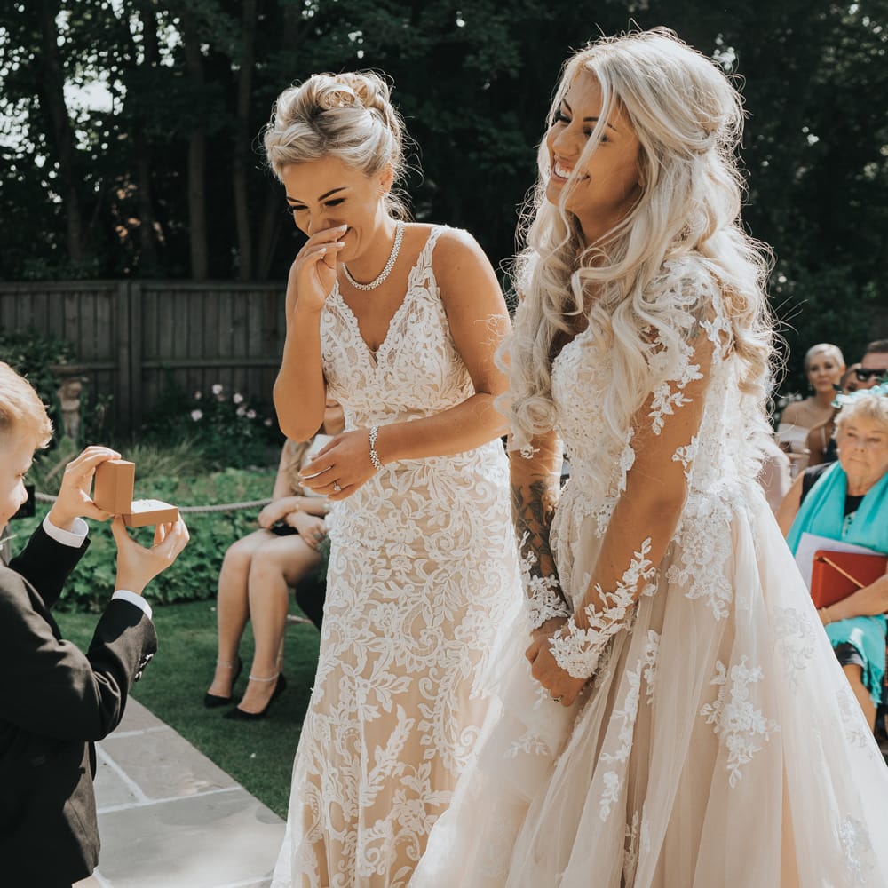 Two brides stand at the altar and are presented with their wedding rings by their son. 