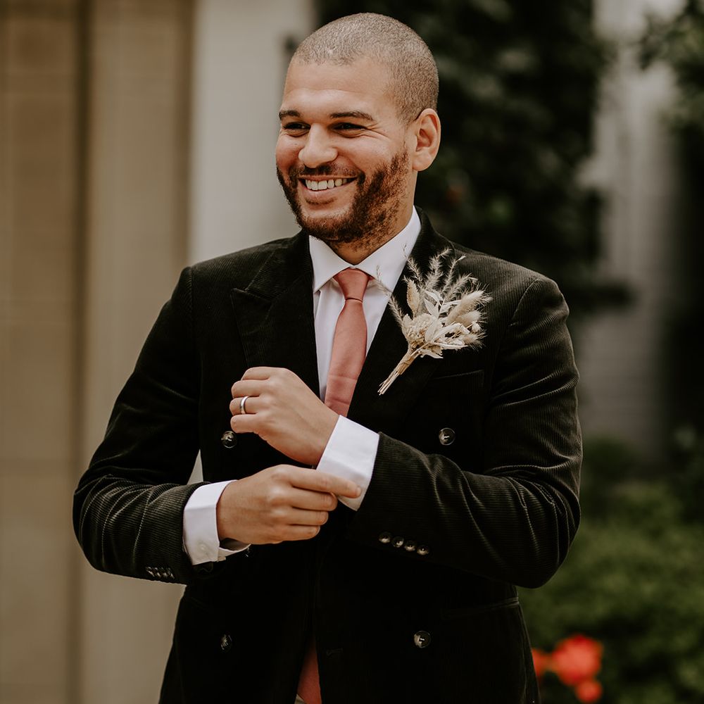Stylish groom in a black cord jacket and dusky pink satin tie with a dried flower buttonhole 