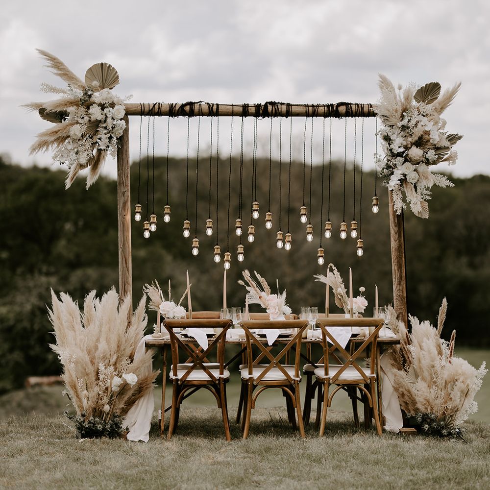 Edison bulb light installation wrapped around a wooden frame decorated in neutral fresh flowers and dried grasses including palm leaves and pampas grass