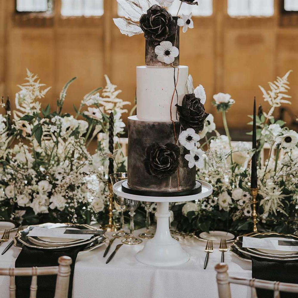 Three tier wedding cake with black and white tiers on a white cake stand decorated with iced flowers 