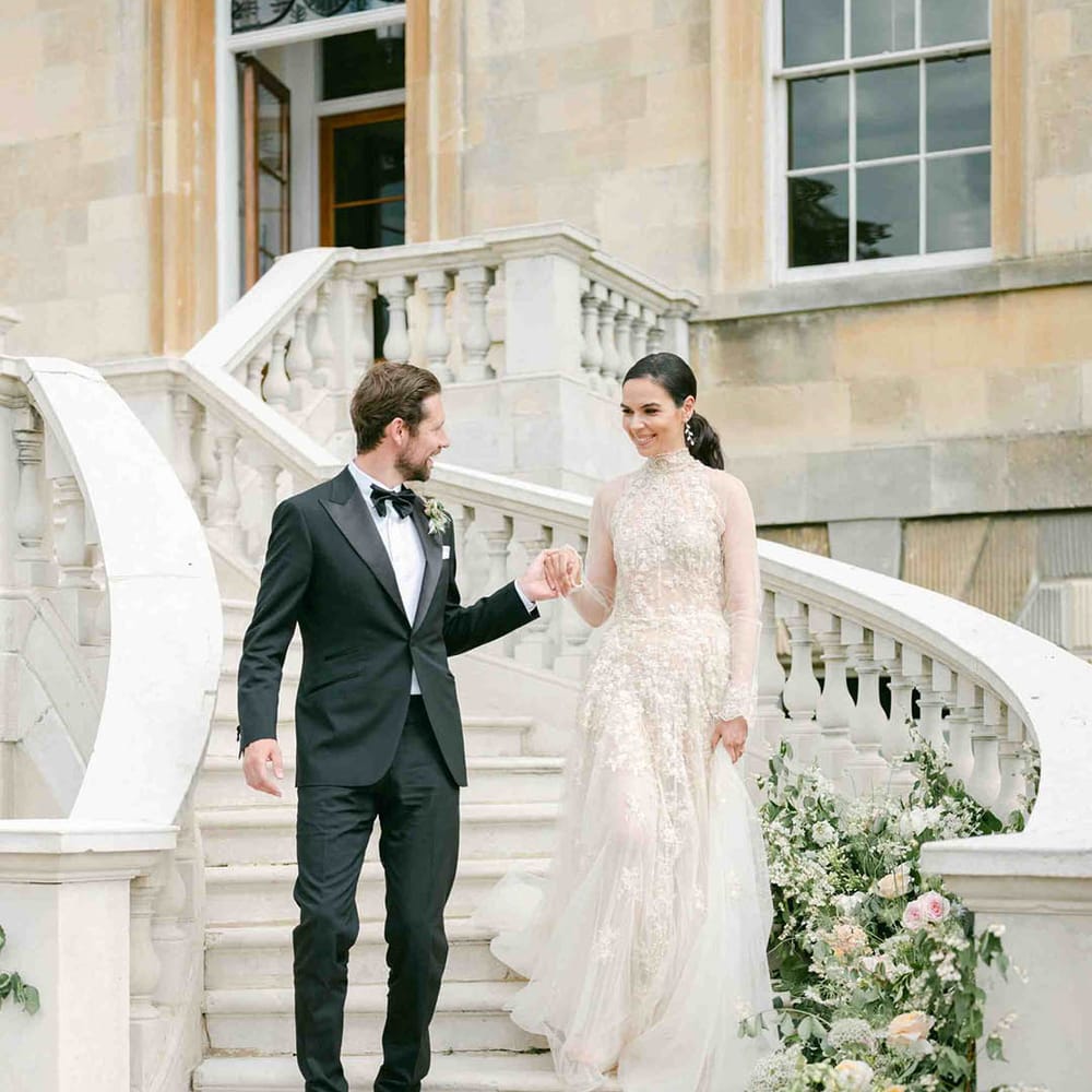 Bride in a romantic lace wedding dress with high neck and long sleeves walking down the stairs at Botley's Mansion with her groom in a tuxedo 