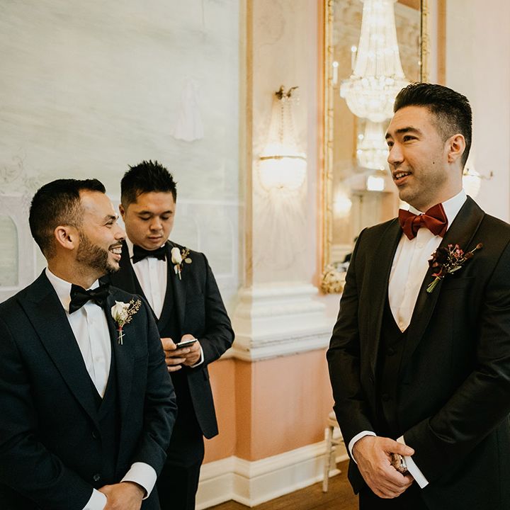 Groom in tuxedo with burgundy bow tie awaits bride's arrival