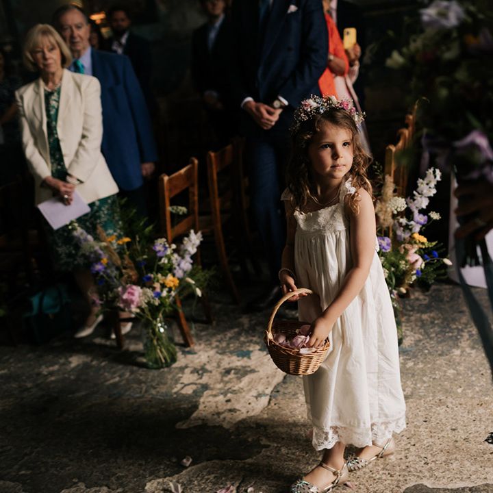 Flower girl in white dress and flower crown throws pink rose petals from a wicker basket 