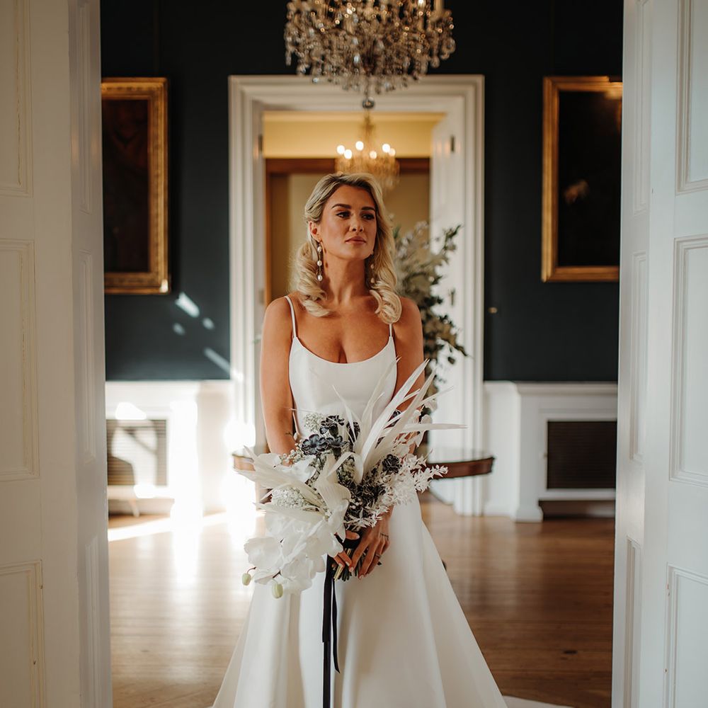 Blonde bride with long wavy hear wearing pearl earrings and holding a dried and fresh flower boqueut with orchids in a princess wedding dress at Hodsock Priory 