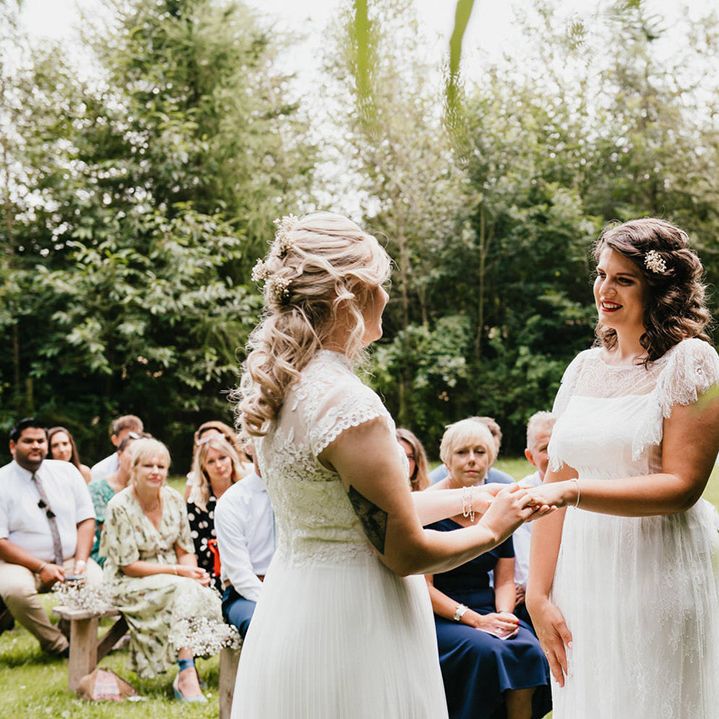 Bride puts the ring on bride's finger at the altar as wedding guests look on during outdoor ceremony