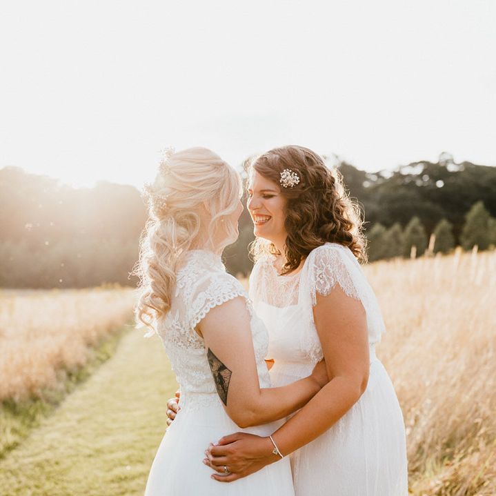 Smiling brides hug each other at golden hour in field 