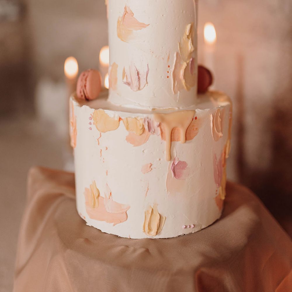 Two tier white buttercream wedding cake with pastel pink and yellow frosting and macaroons 