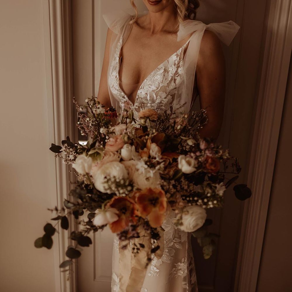 Bride in v neck lace Made With Love wedding dress with bow sleeves and autumnal wedding bouquet 