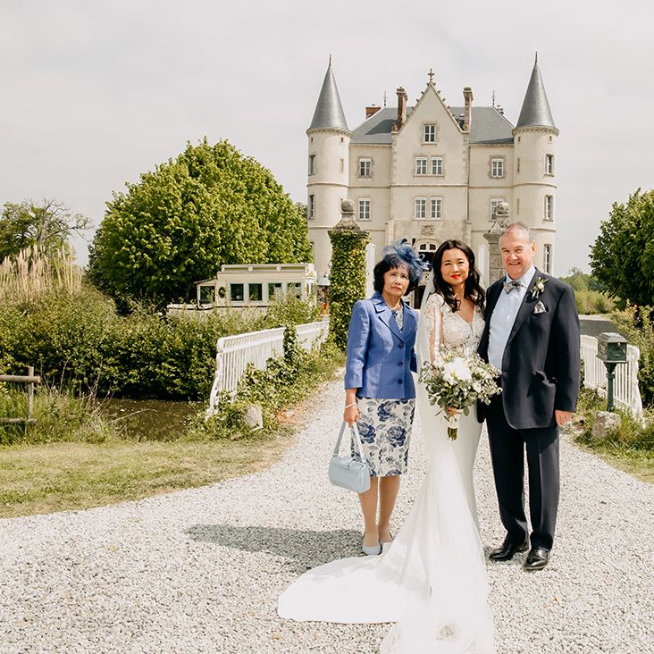 Bride poses in front of the chateau with mother and father in wedding attire for the big day 