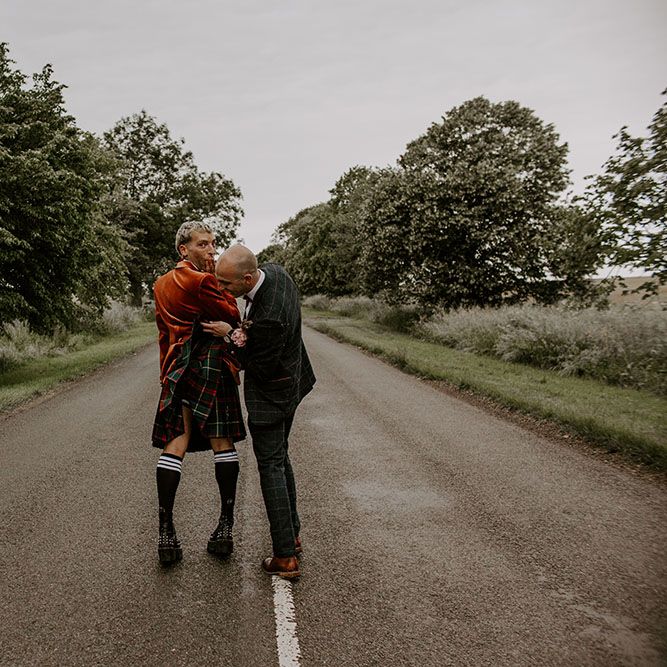 Groom cheekily lifts kilt of his groom outdoors as they walk through the street on their wedding day