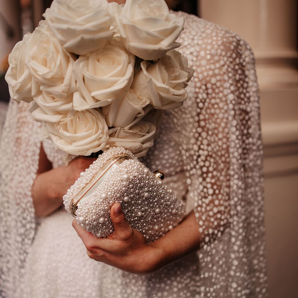 Bride holding her white rose bouquet and pearl clutch bag for classic style hotel wedding 