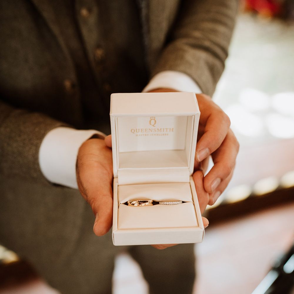 White ring box holding the groom's gold wedding ring and bride's diamond gold wedding band 