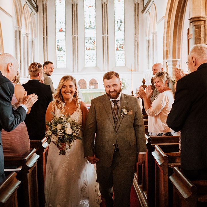 Bride and groom walk back down the aisle as the wedding guests stand and applaud 