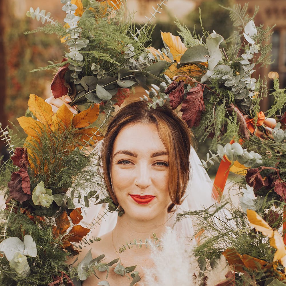 Bride wears red lipstick and is surrounded by colourful Autumnal flowers 