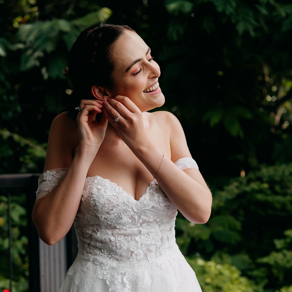 Bride in off the shoulder lace wedding dress with sweetheart neckline and lace floral details adjusting diamond drop earrings