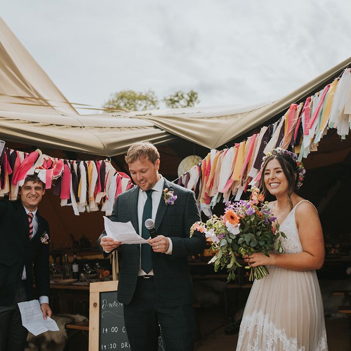 Groom gives speech beside his bride in front of colourful bunting 
