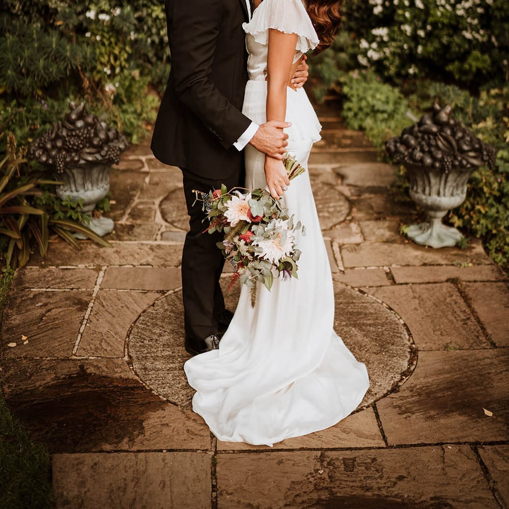 Groom in classic black tuxedo with black bowtie kissing bride in v neck satin wedding dress with sheer butterfly sleeves on the cheek
