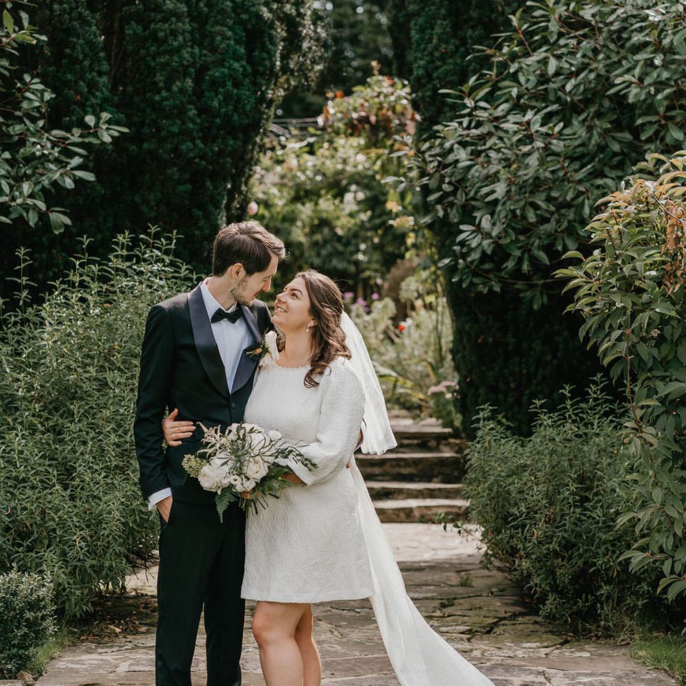 The bride wearing short block heel white shoes smiles up at the groom in black tux for their couple portraits 