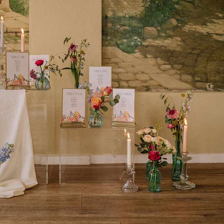Botanical luxe wedding stationery and decor on large glass stands with tapered candles in glass candlestick holders and white tablecloths 