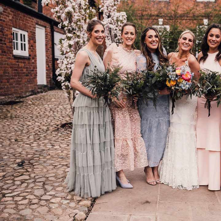 Bridesmaids in dainty light floral mismatched bridesmaid dresses holding mixed wildflower bouquets at greenery themed wedding