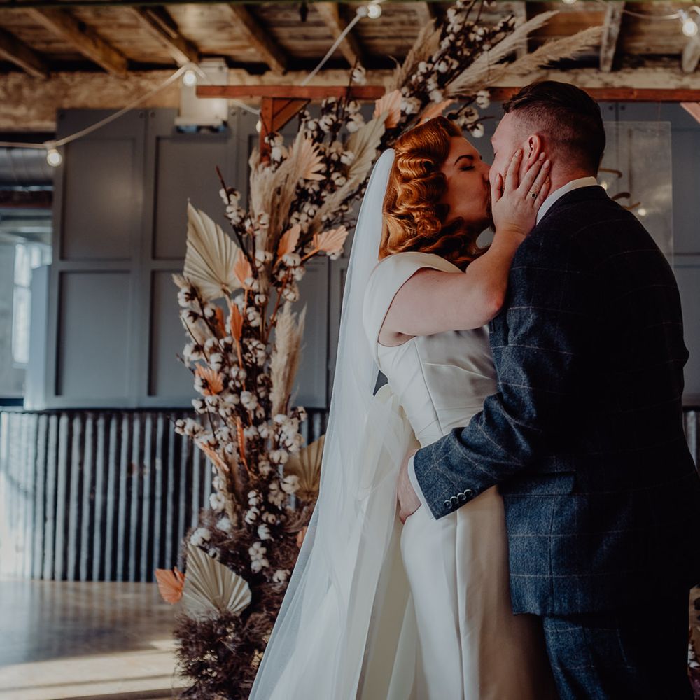 Bride with vintage wedding hair kissing her groom at the dried flower altar