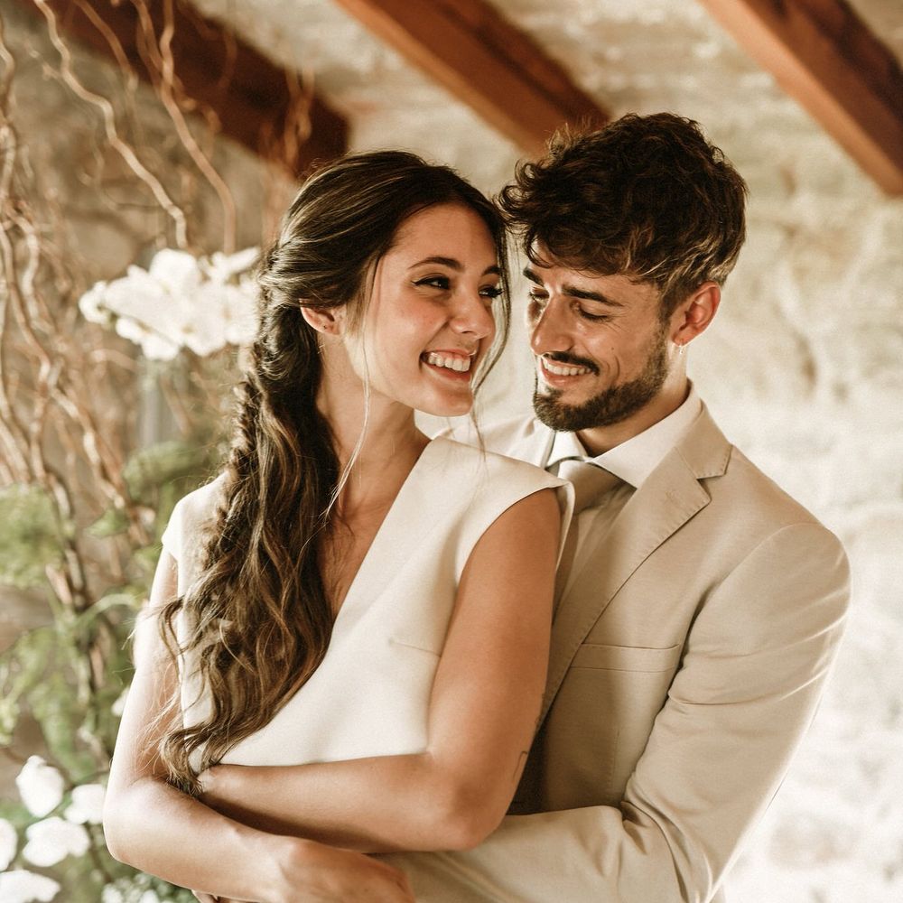 Bearded groom in a beige suit embracing his bride in separates with a long braided half up half down wedding hairstyle