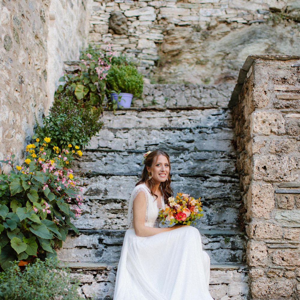 The bride sitting on steps at Valeni Boutique Hotel in Greece wearing Vasia Tzotzopoulou