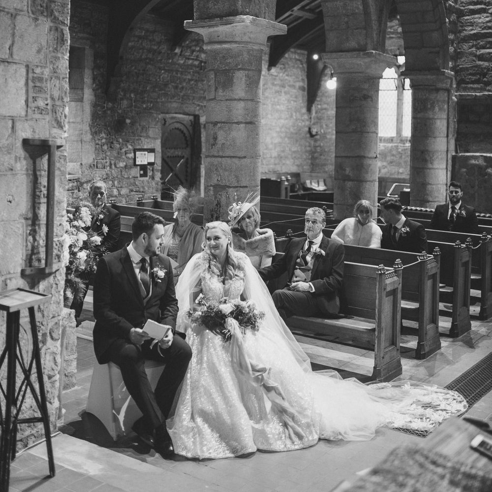 Bride in a princess wedding dress and bridal cape sitting at the altar with her groom in a navy suit 
