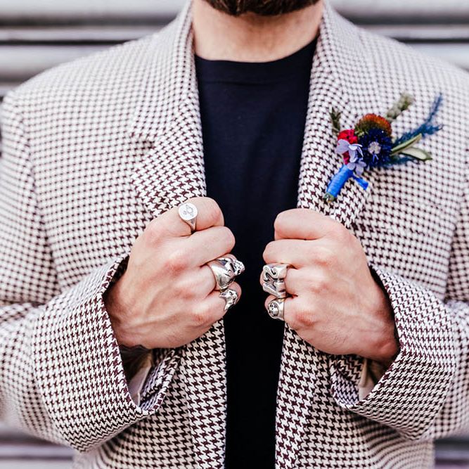 Groom in a dogtooth jacket wearing rings holding onto his lapels 